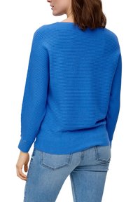 Blå stickad tröja med ribbad textur, rund hals och långa ärmar. Återfinns tillsammans med ljusblå jeans som har en avslappnad passform och en ledig stil.