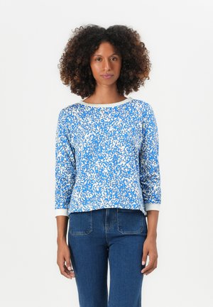 Blåmönstrad långärmad T-shirt med rund halsringning och vita detaljer vid ärmsluten, tillverkad av ett mjukt tyg. Bärs med jeans.