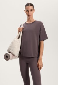 Oversized mauve T-shirt och matchande leggings. Modellen håller en krämfärgad tygväska och en rullad yogamatta med rosa ränder.