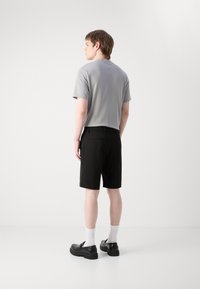 T-shirt gris à manches courtes avec un col rond, associé à un short noir. Le mannequin se tient de dos, portant des chaussures noires à enfiler et des chaussettes blanches.