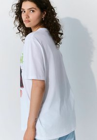Hvid bomulds t-shirt med grafisk tryk på fronten, oversized pasform og korte ærmer. Glat tekstur med en afslappet silhuet.