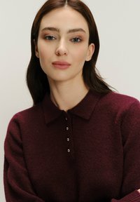 Bordové pletené polo svetr s límečkem a čtyřmi ozdobnými knoflíky, s měkkým, texturovaným povrchem a uvolněným střihem.