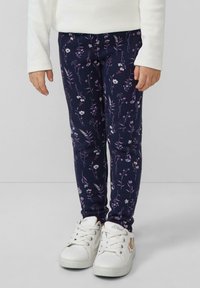 Granatowe legginsy w kwiaty z wzorem małych białych i fioletowych kwiatków, wykonane z miękkiego, elastycznego materiału, zestawione z białymi sneakersami.