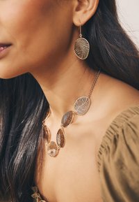 Gold leaf-patterned necklace and matching earrings feature intricate detailing and a shiny finish, enhancing their elegant design.