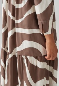 Brown and white patterned dress with a fluid fabric, featuring flowing sleeves, a tiered design, and side slits near the cuffs.