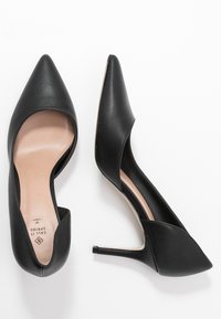 Escarpins noirs à talon haut avec un bout pointu, finition en cuir lisse, côtés ouverts et un talon fin. L'intérieur est orné d'une doublure beige clair.