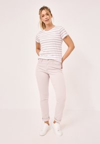 Weiß gestreiftes T-Shirt, blassrosa enges Jeans und weiße Turnschuhe. Das T-Shirt hat kurze Ärmel, die Jeans haben hochgekrempelte Säume und Fronttaschen.