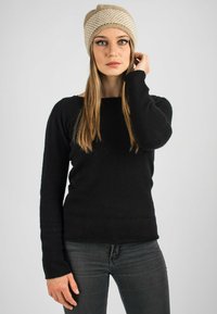 Maglione nero a maglia con maniche lunghe, caratterizzato da un scollo quadrato; abbinato a jeans grigio scuro. Il modello indossa un berretto a righe beige.