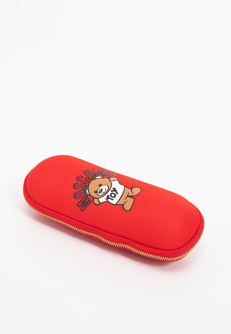 Rotes rechteckiges Brillenetui mit texturiertem Oberflächen, das einen Cartoon-Bären und "Moschino Toy" in fetten Buchstaben zeigt. Mit goldenen Reißverschlussdetails.