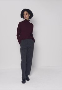 Vínový rolák spojený s texturovanými šedými kalhotami s širokými nohavicemi a černými botami, na jednobarevném pozadí.