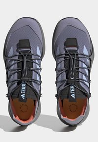 Sapatos de trail running em malha cinza e preta com detalhes reflexivos. Apresentam atacadores elásticos e solas texturizadas. Design ecológico.