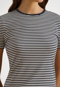 Sieviete tērpusies tumši zils un balts horizontāli svītrains īsroku krekls ar apaļu kakla izgriezumu, kas beidzas zem pleciem.