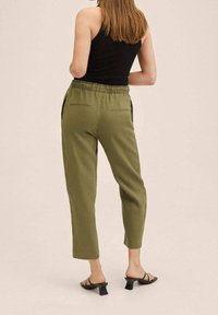 Oliwkowe spodnie o luźnym kroju, z elastycznym paskiem w talii i bocznymi kieszeniami. Noszone z czarnymi sandałami i dopasowanym czarnym topem.