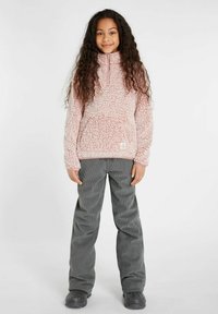 Rosa, flauschiger Fleece-Pullover mit halbem Reißverschluss und Fronttasche, kombiniert mit grauen Cordhosen. Das Outfit zeichnet sich durch eine lässige Passform und strukturierte Stoffe aus.