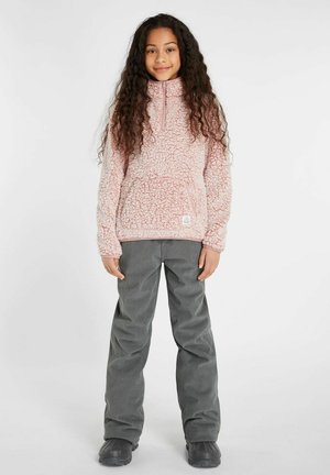 Pullover in pile rosa e morbido con zip metà e tasca frontale, abbinato a pantaloni in corduroy grigi. L'outfit presenta una vestibilità comoda e tessuto testurizzato.