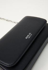 Zwarte leren clutch tas met een zilveren schouderband en het logo "REPLAY SINCE 1981" geperst op de klep.