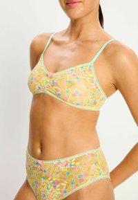 Ensemble de lingerie en dentelle jaune avec des motifs floraux, ornements bleu clair et détails délicats. Comprend un bralette avec des bretelles réglables et des culottes assorties.