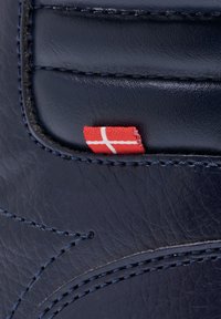 Dunkelblaues Leder nahaufgenommen mit kontrastierendem blauen Stich und einem kleinen roten Etikett mit einem weißen Kreuz, das auf dänischen Ursprung hinweist.
