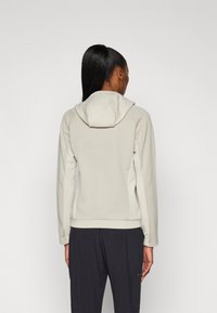 Lichtgrijze hoodie met een slim fit ontwerp, zachte stof en een capuchon. Lange mouwen en een gladde textuur, gecombineerd met donkere broeken.