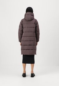 Lang, gewatteerde jas in donker mauve met een capuchon, met horizontale stiksels en een rechte snit, gecombineerd met een zwarte rok en schoenen.