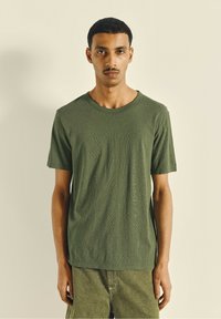 Olive green short-sleeved crewneck t-shirt featuring a textured fabric and a relaxed fit, paired with matching green shorts.