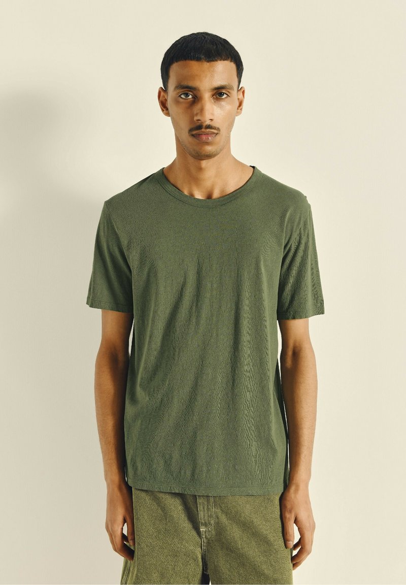 Olive green short-sleeved crewneck t-shirt featuring a textured fabric and a relaxed fit, paired with matching green shorts.