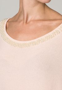 Maglione lavorato a maglia di un leggero rosa, con un ampio scollo rotondo decorato da un insieme di piccoli dettagli in perle iridescenti.