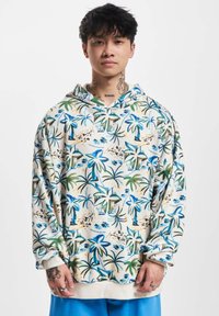 Sudadera con capucha en color crema con estampados de palmeras tropicales en azul y verde. Cuenta con un bolsillo frontal y un ajuste relajado.