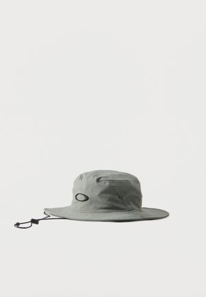 Chapeau bob à large bord gris clair avec sangle de menton réglable et logo ovale noir à l'avant, présenté sur un fond blanc.