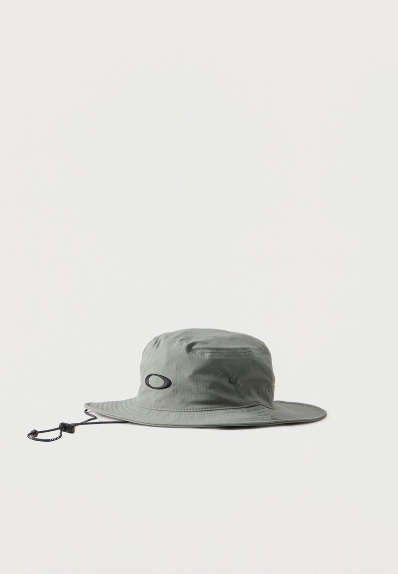 Chapeau bob à large bord gris clair avec sangle de menton réglable et logo ovale noir à l'avant, présenté sur un fond blanc.