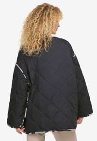 Quiltet sort jakke med løs pasform, der har et diamantmønster, brede ærmer og en kontrastfarvet mønstret foering ved kanterne.