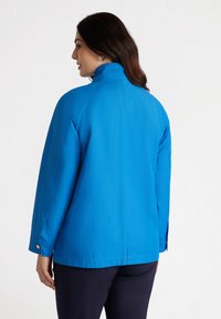 Niebieska wodoodporna kurtka z wysokim kołnierzem, zapinanymi mankietami i gładką fakturą; cechuje się prostym krojem i detalami na szwie z tyłu.