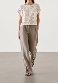 Haut court en dentelle crème avec des motifs floraux délicats, associé à un pantalon large en lin gris clair et des tongs noires.