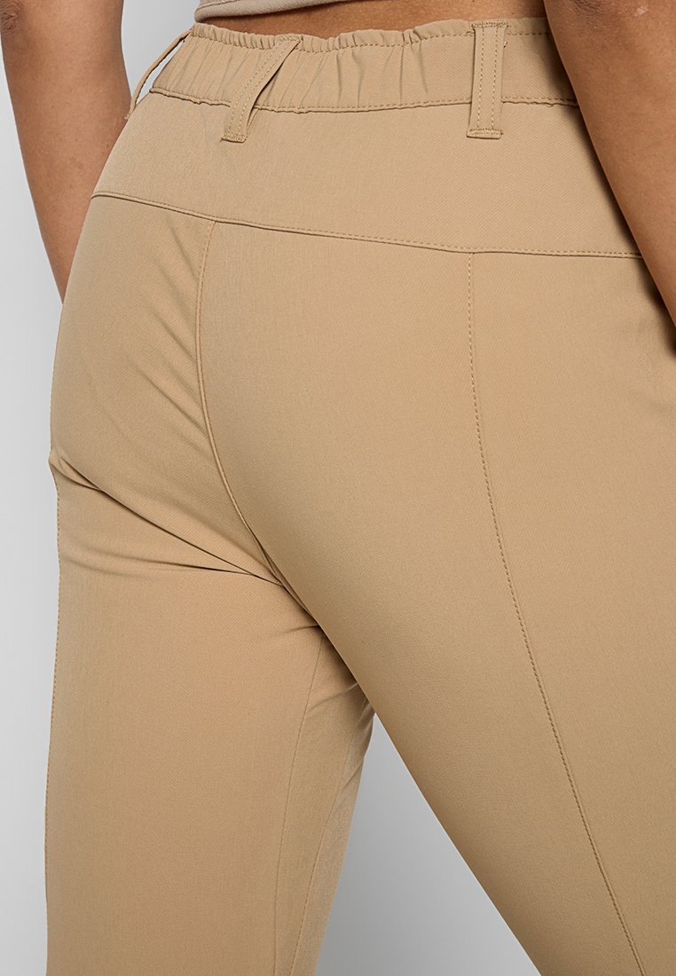 Beżowe legginsy z wysokim stanem i elastycznymi detalami, o gładkiej fakturze i minimalnym przeszyciu, co zapewnia schludny wygląd.