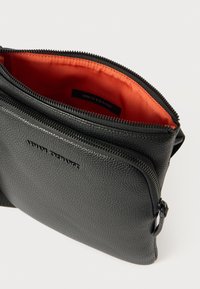 Čierna kožená taška s textúrou a oranžovým podšívaním, s uzáverom na zips a embosovaným logom "ARMANI EXCHANGE" na prednej strane.