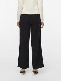 Zwarte, wijde broek met een gladde textuur, gecombineerd met een aangesloten crèmekleurige trui. Minimalistisch ontwerp zonder zichtbare patronen of hardware.