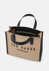 Sac tissé beige texturé avec poignées et accents en cuir noir ; dispose d'une poche intérieure zippée et d'un logo de marque en relief sur le devant.