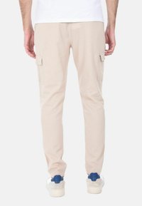 Pantaloni cargo beige con tasche laterali, vestibilità affusolata e texture liscia. Indossati con sneakers bianche con accenti blu.