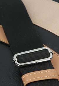Banda in tessuto nero con una fibbia d'argento lucida, accentuata da un particolare in pelle color cuoio e cuciture in contrasto su uno sfondo scuro e strutturato.