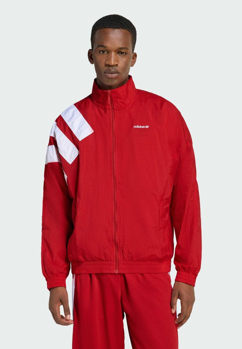 Červená vetrovka s bielymi akcentmi na ľavom pleci a vyšitým logom na hrudi; priliehavé manžety a spodný lem.