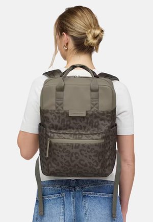 Woman with blonde hair in a bun wearing a two-tone gray backpack with leopard print and a front zipper pocket, white shirt, and blue jeans.