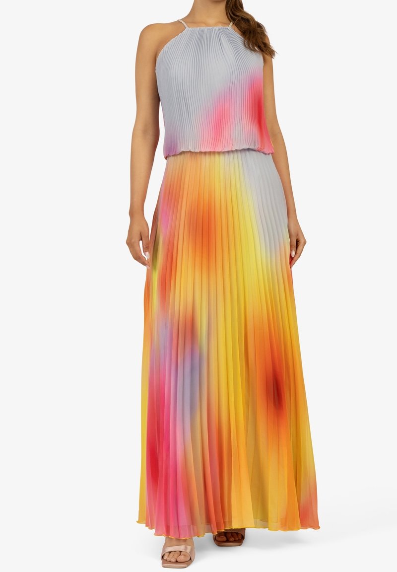 Femme portant un haut plissé sans manches à col halter et une longue jupe assortie avec un motif coloré jaune, rose, orange et violet.