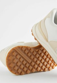 Jasne buty sportowe z teksturowaną gumową podeszwą i siateczkowymi detalami. Posiadają amortyzowaną podeszwę środkową i minimalistyczny design.