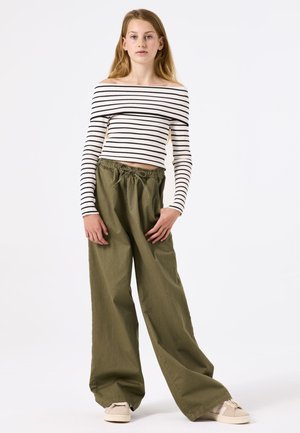 Top de hombros descubiertos a rayas en blanco y negro, combinado con pantalones holgados verde oliva con cinturilla elástica. Zapatillas beige completan el look.