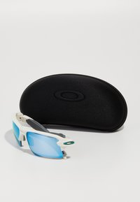 Oakley-Sonnenbrillen mit einem weißen Rahmen, blauen, spiegellosen Gläsern und grauen Akzenten, begleitet von einem schwarzen Hartschalenetui mit dem Oakley-Logo.