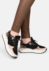 Baskets noires et dorées avec des accents en maille et texturés, semelle blanche épaisse, détails de lacets complexes et un mélange de matériaux lisses et brillants.