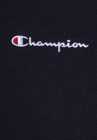 Zwart katoenen stof met een gestructureerde weving; heeft een geborduurd "Champion" logo in het wit en rood in de linkerbovenhoek.