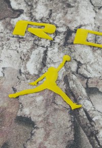 Κίτρινο λογότυπο μπάσκετ Jumpman και μερικώς έντονα κίτρινα γράμματα σε γκρι, υφής πέτρας υπόβαθρο.