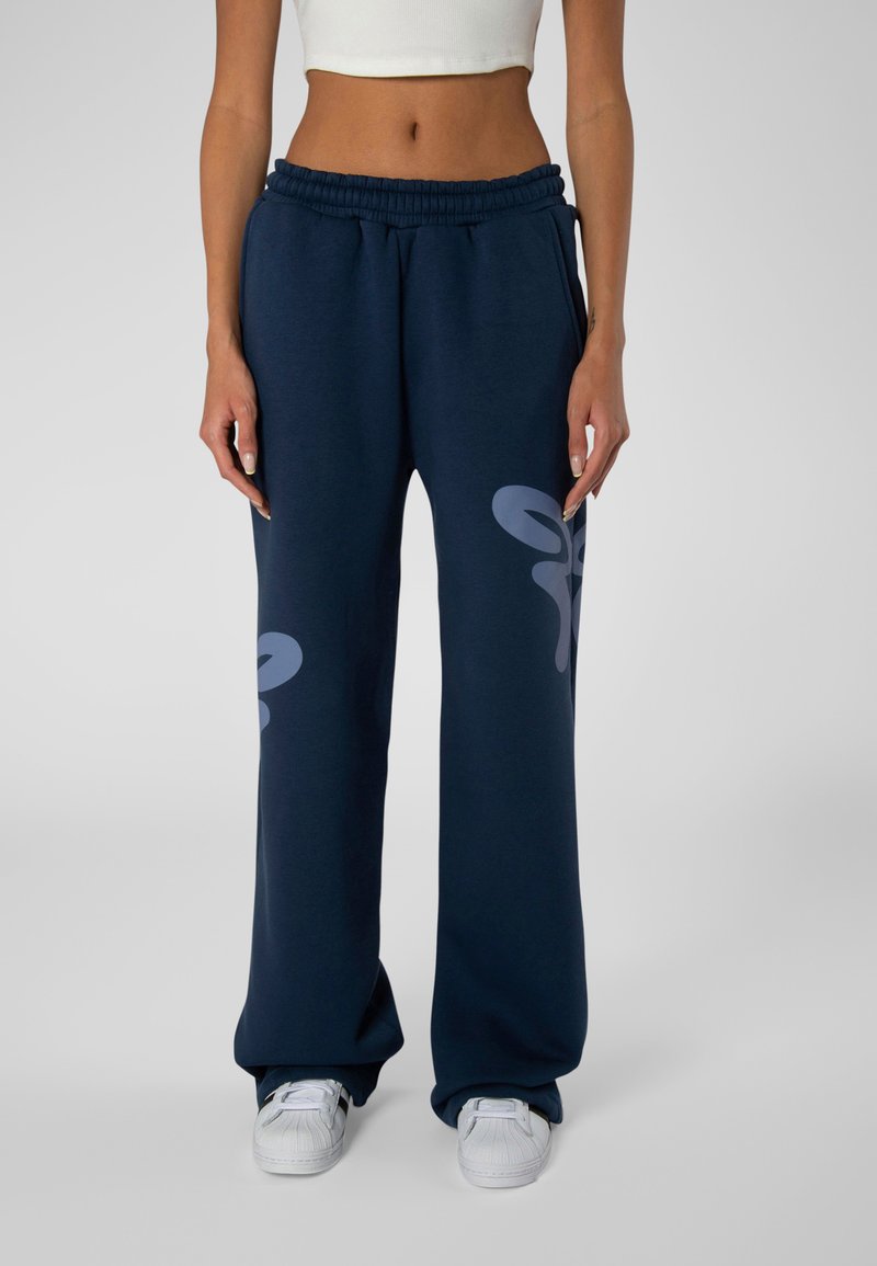 Marineblaue Sweatpants mit elastischem Bund, weiten Beinen und hellgrauen abstrakten Mustern auf der rechten Seite. Weicher, strukturierten Stoff.