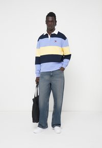 Maglietta polo a maniche lunghe a righe colorate con righe blu chiaro, gialle e navy, colletto bianco e logo. Abbinata a jeans a gamba larga blu chiaro.